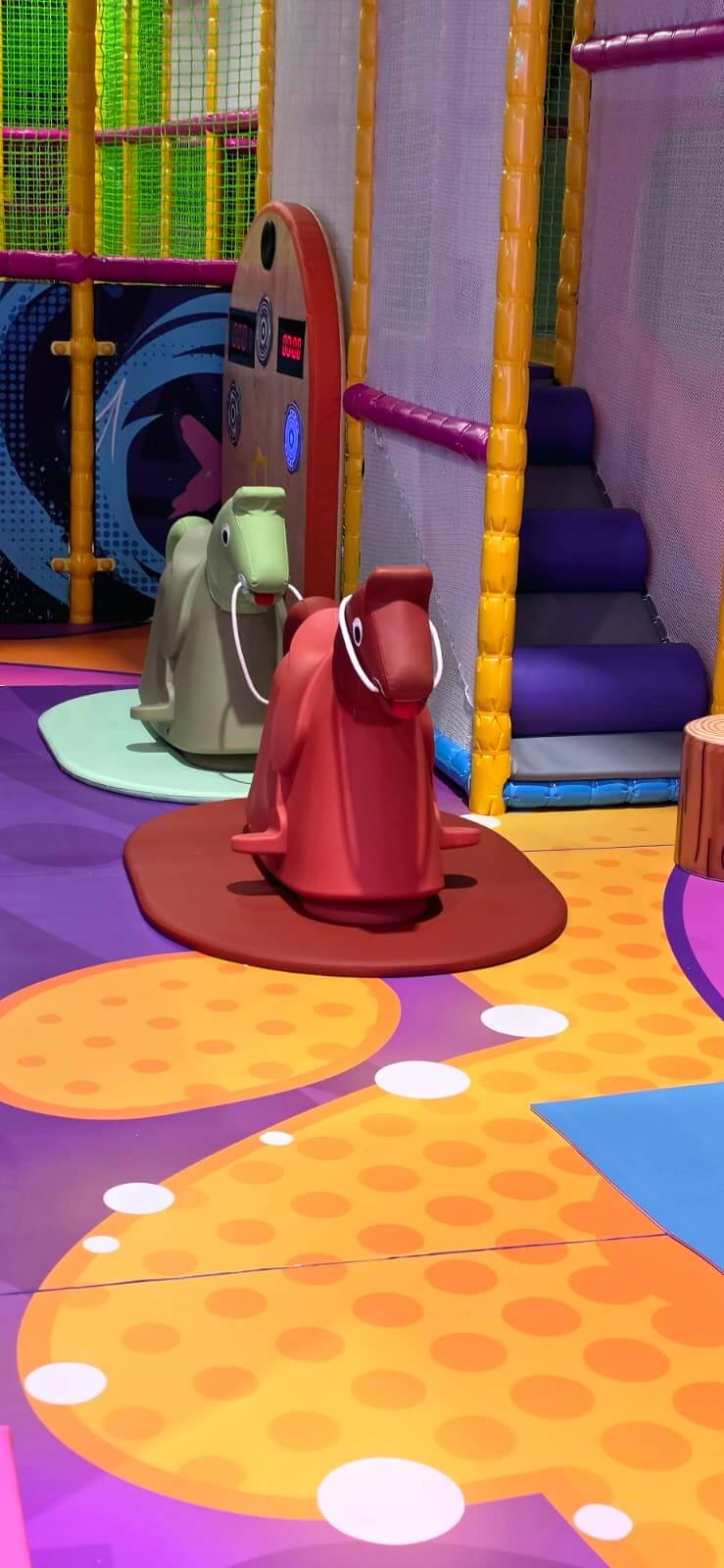 Plastic horse rocking toys on a soft padded patterned floor inside the Playtopia Burlington toddler area.