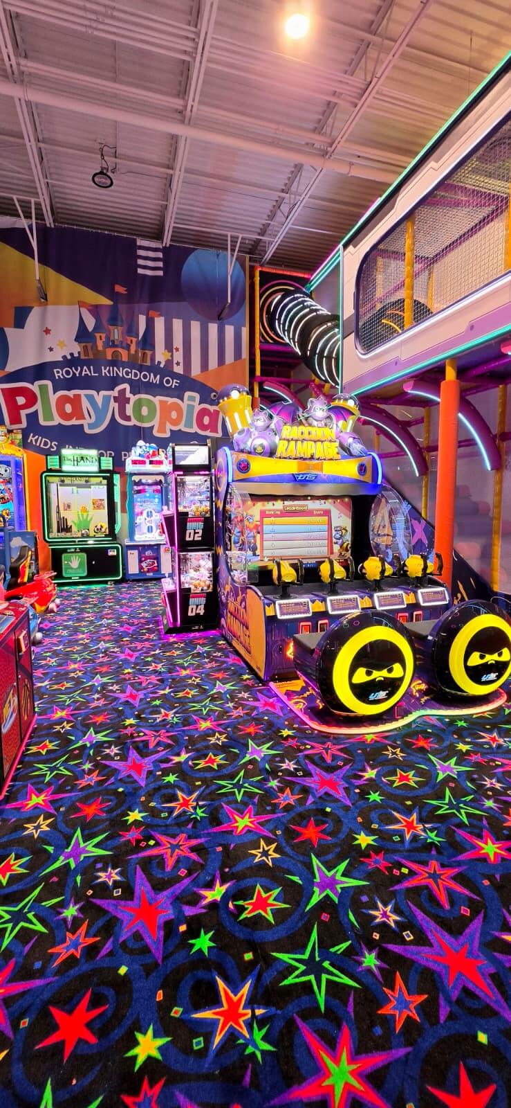 An aisle of interactive kids arcade basketball shooting games and ticket redemption stations with star-patterned carpet floor inside Playtopia.