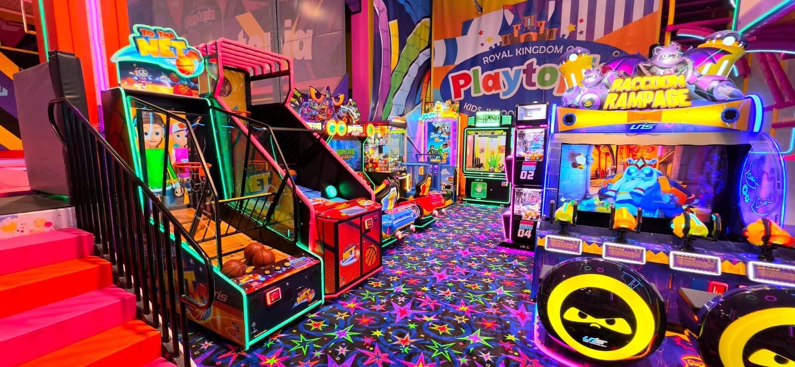 An aisle of interactive kids arcade basketball shooting games and ticket redemption stations with star-patterned carpet floor inside Playtopia.