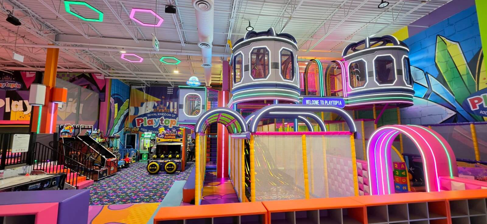 Wide view of the 3-storey indoor jungle gym play structure with neon accents and climbing areas at Playtopia.